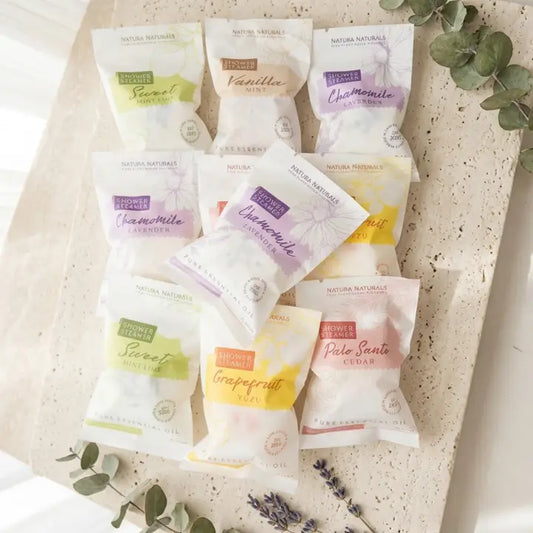 Nine small pouches of Nature's Natural Lavender & Tea Tree Hand Sanitizer in assorted scents, arranged on a textured beige stone surface with decorative greenery.